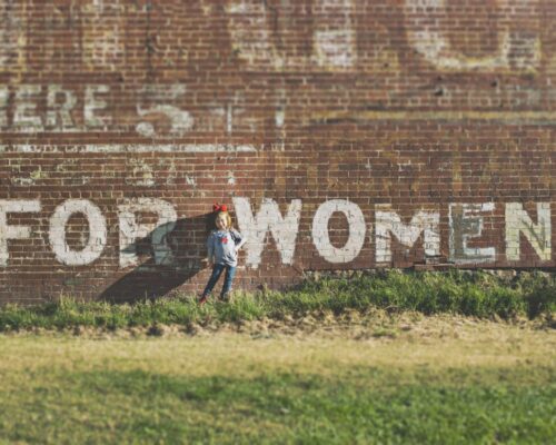 young girl standing in front of wall saying for women